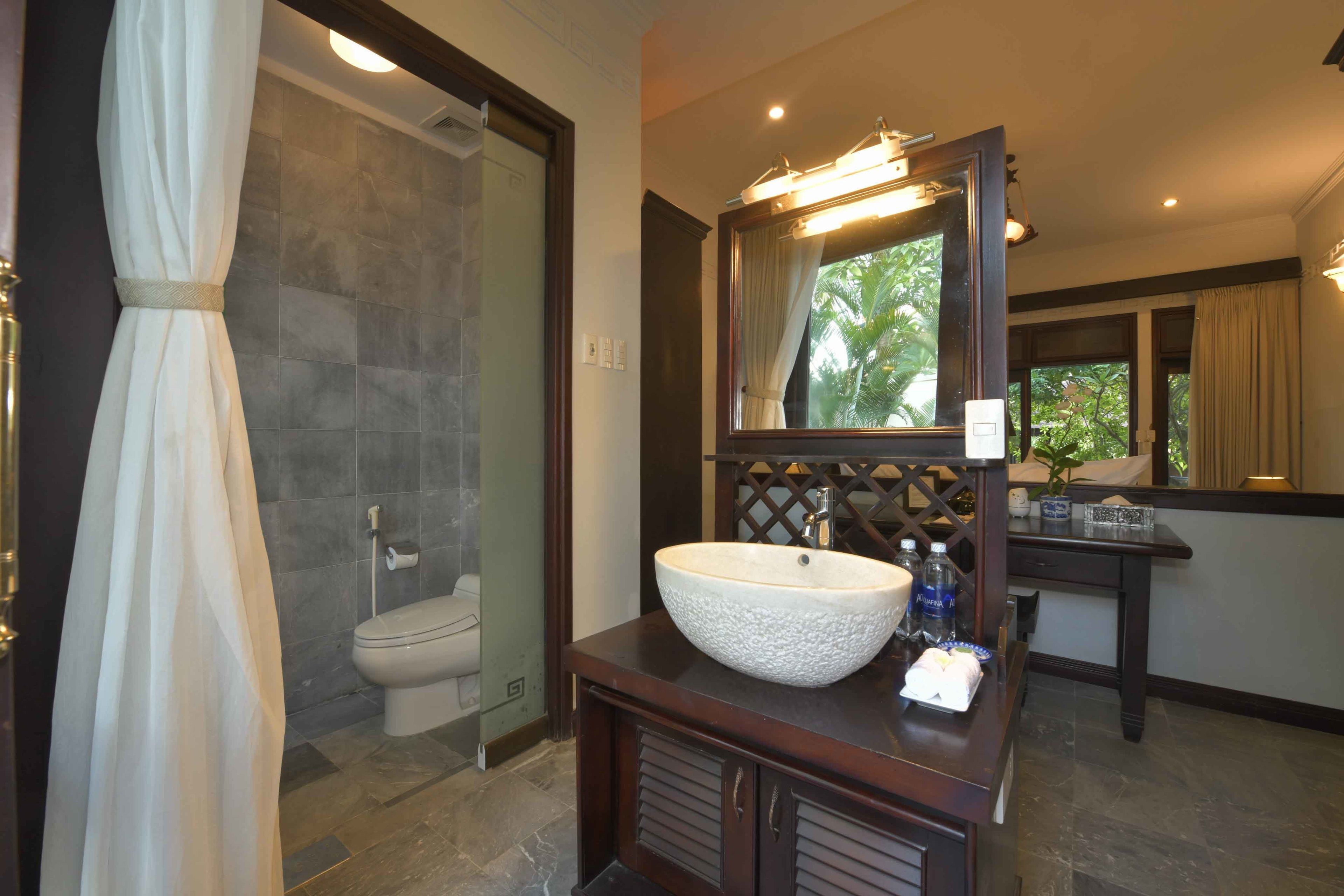 Un baño con un lavamanos grande de color blanco, un espejo, un inodoro y una zona de ducha.