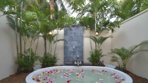 A spa area with a hot tub surrounded by tropical plants and a stone wall. - Villa Hoa Su - Frangipani Village Resort (Da Nang)