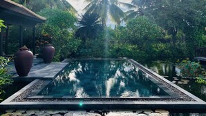 A rectangular pool with a stone border, surrounded by lush greenery and palm trees. - Villa Hoa Su - Frangipani Village Resort (Da Nang)