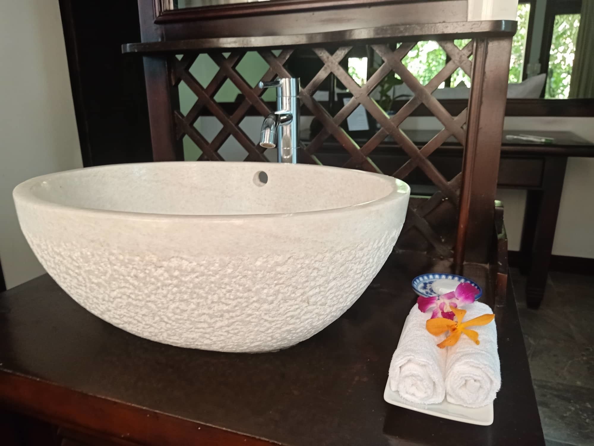 A large white ceramic bowl sink on a dark wooden table with a decorative lattice partition in the background.