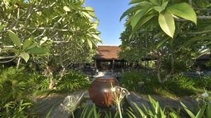 A garden with a central water feature, surrounded by lush greenery and a covered structure in the background. - Villa Hoa Su - Frangipani Village Resort (Da Nang)