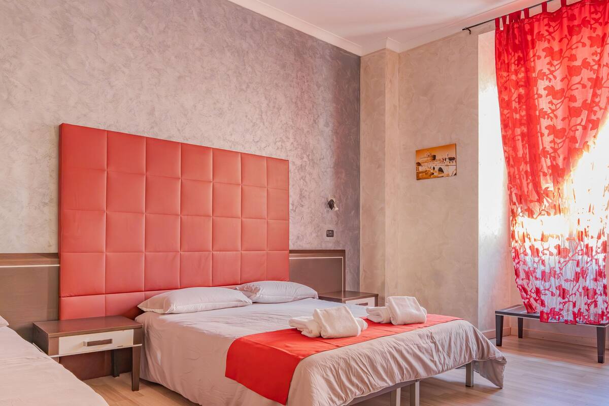 Una habitación de hotel moderna con una cama grande, una mesita de noche, un escritorio y una ventana con cortinas rojas.