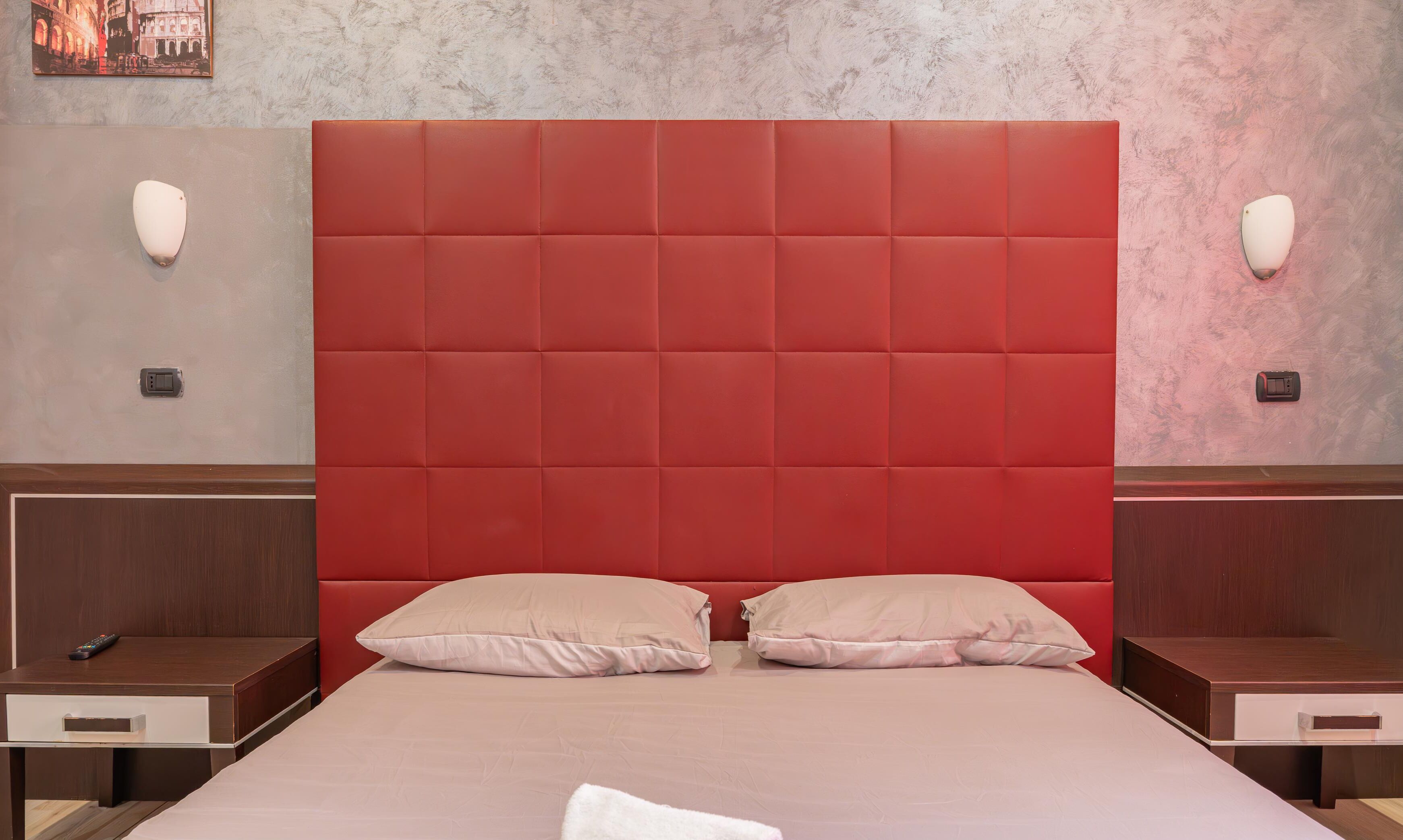 Une chambre d’hôtel avec un grand lit, deux tables de chevet et une tête de lit rouge.