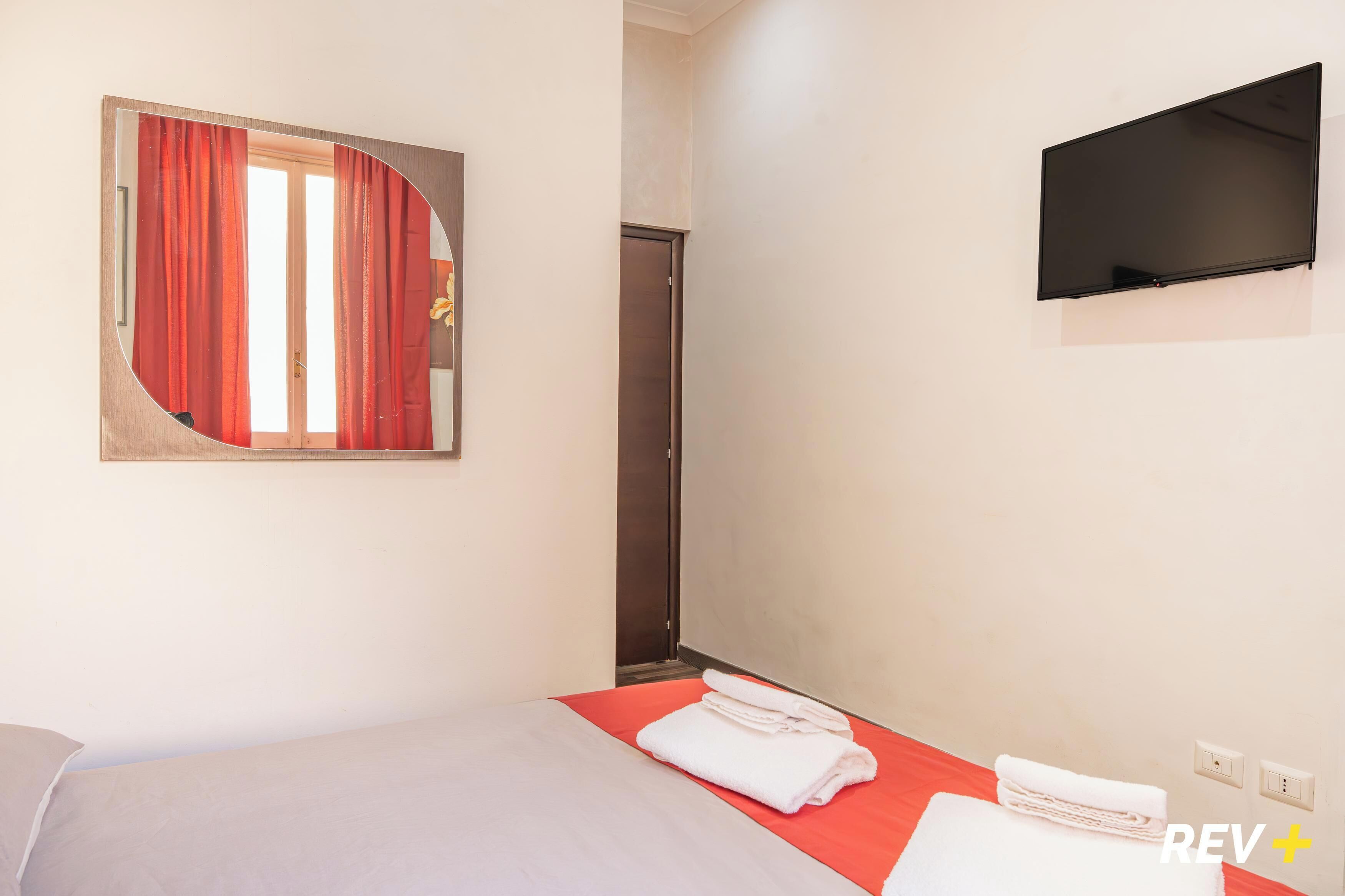 Ein Hotelzimmer mit einem Bett, einem roten und weißen Streifenrollo, einem angebrachten Fernseher und einem Handtuchhalter.