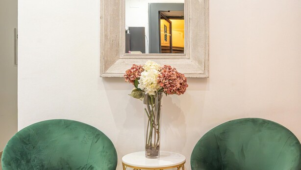 Two green upholstered chairs with gold wire legs, a small white table with a gold wire base, and a vase with flowers. - New Inn (Rome)