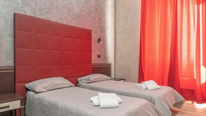 A hotel room with two beds, each with a red headboard and grey bedding. There is a red curtain on one side and a wooden floor. - New Inn (Rome)