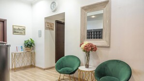 A hallway with two green chairs, a small table with a vase of flowers, a clock, and a framed mirror on the wall. - New Inn (Rome)