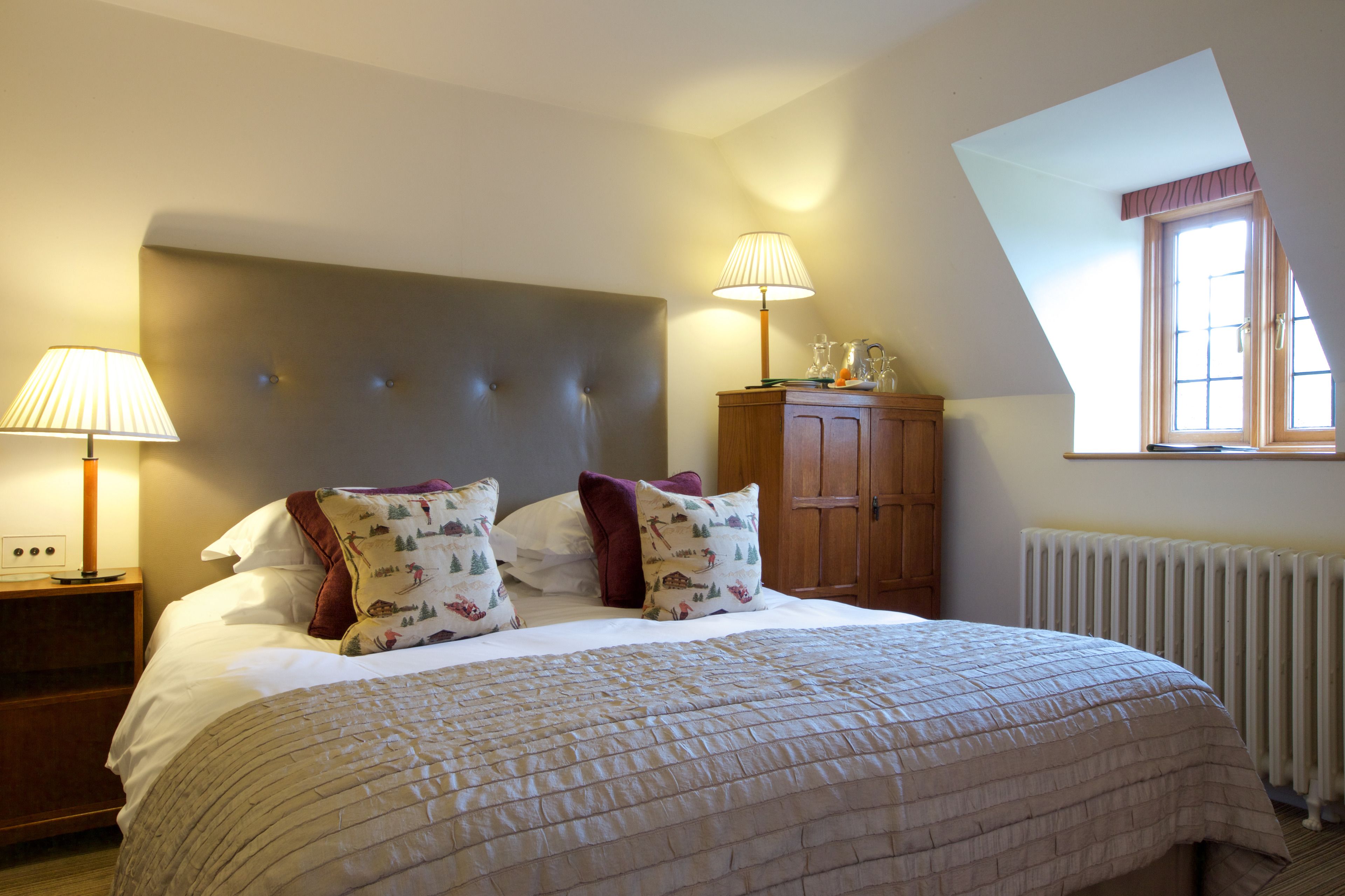 A bedroom with a large bed, two bedside lamps, a wooden cabinet, and a window with a view.