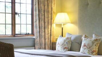 A hotel room with a large bed, a chair, a window with curtains, a lamp, and a headboard.