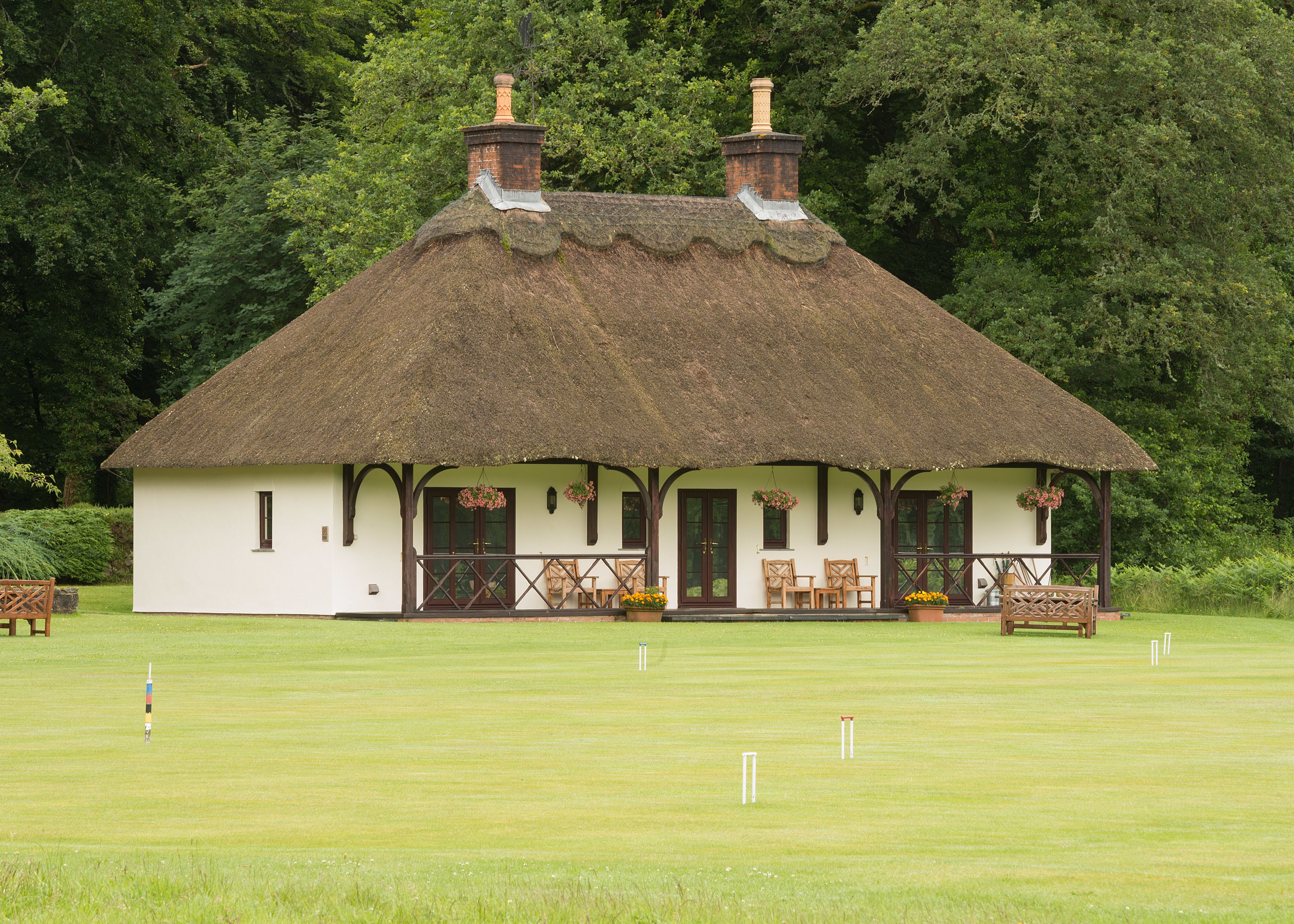 A thatched-roof cottage with a porch, wooden furniture, and flower boxes.