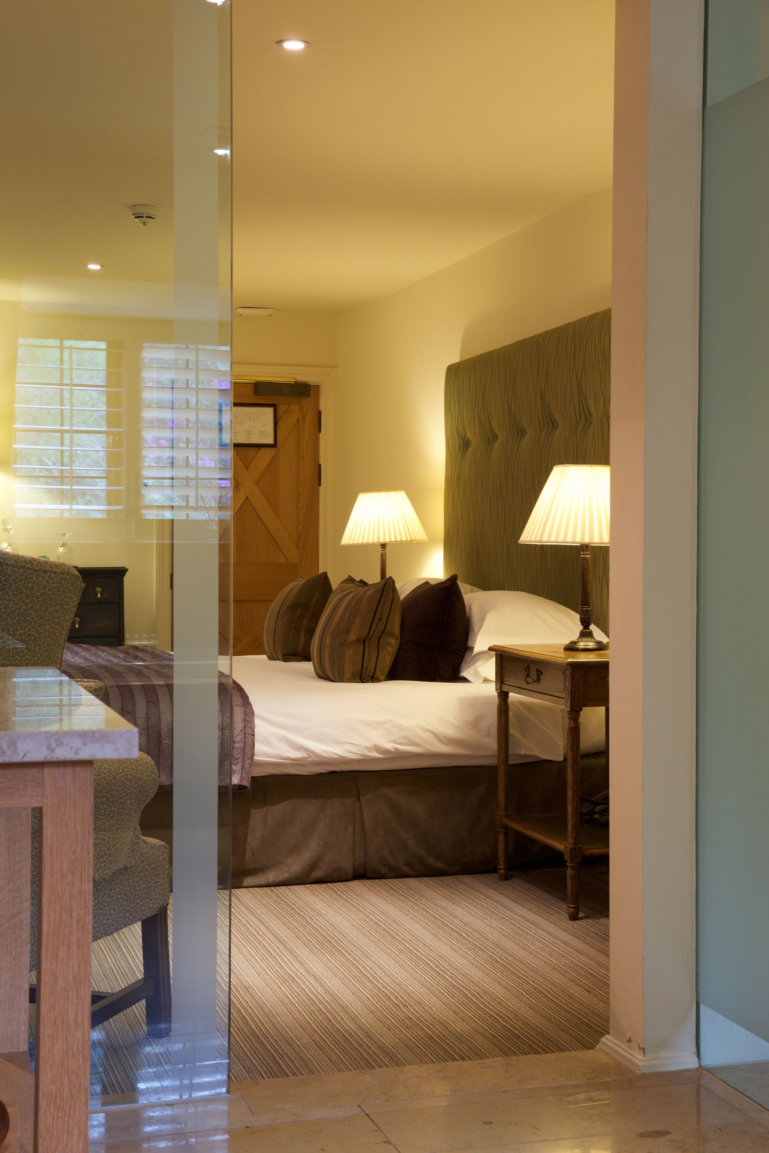 A hotel room with a bed, two bedside lamps, a wooden headboard, a nightstand, and a chair.