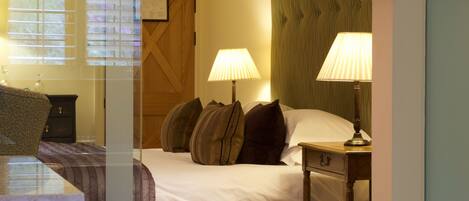 A hotel room with a bed, two bedside lamps, a wooden headboard, a nightstand, and a chair.