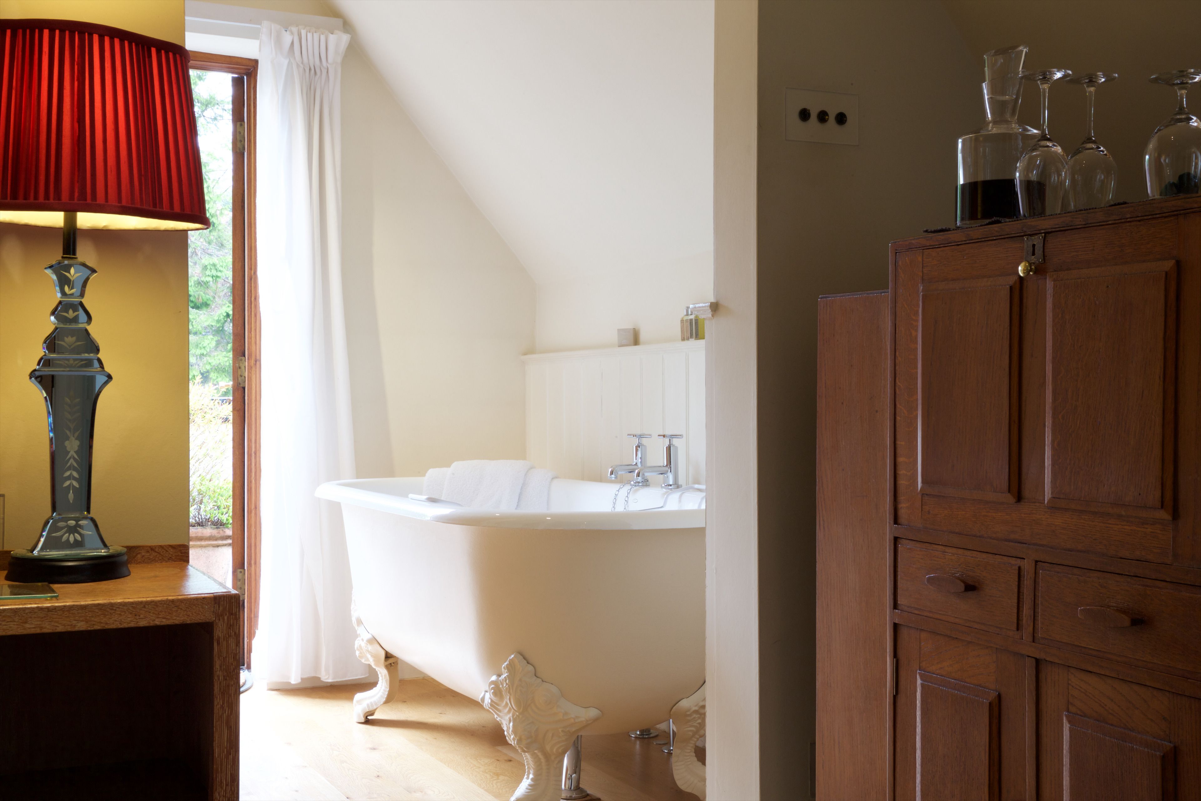 A bathroom with a clawfoot bathtub, a wooden cabinet, and a lamp.