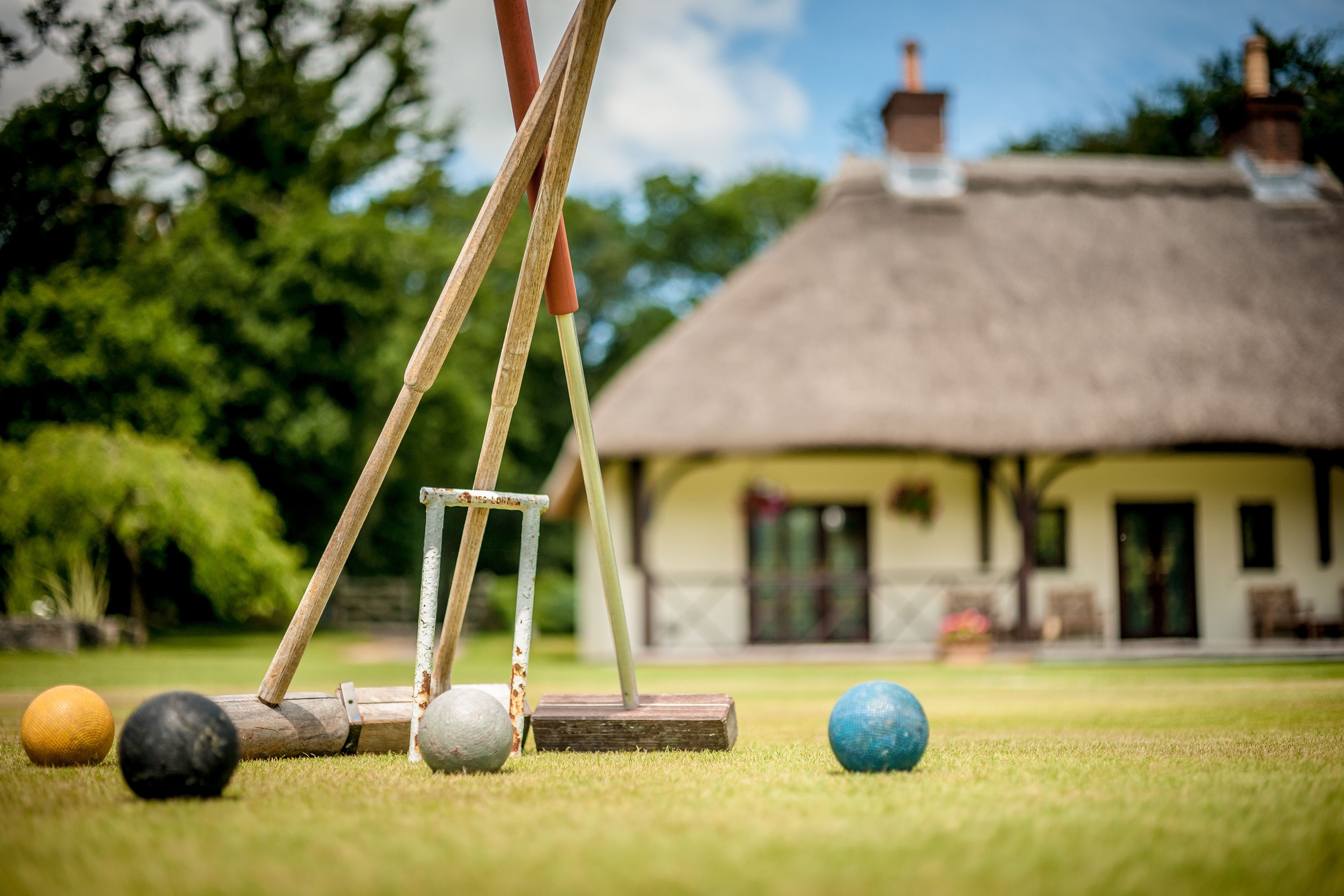 A croquet set on a lawn with a thatched-roof building in the background.