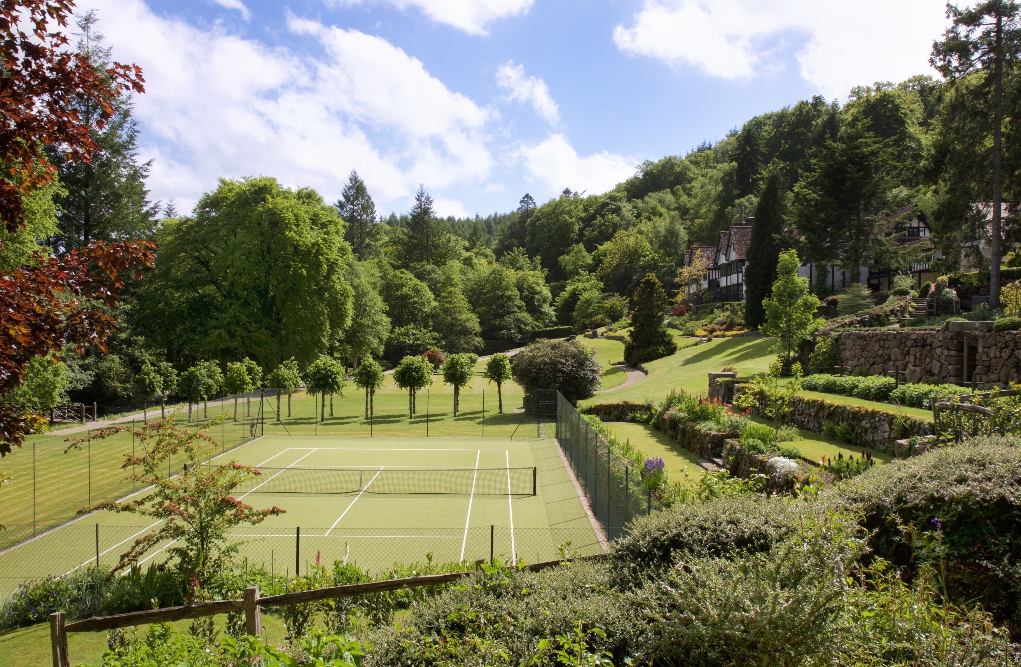 Un court de tennis entouré d’une végétation luxuriante et de murs en pierre.
