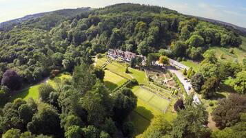 An aerial view of a large estate with a tennis court, landscaped gardens, and a variety of trees.