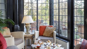 A conservatory with wicker furniture, a table with tea sets, and a view of greenery outside. - Gidleigh Park (Newton Abbot)