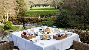 A table set outdoors with various food items and tea, overlooking a scenic landscape with trees and a grassy field. - Gidleigh Park (Newton Abbot)