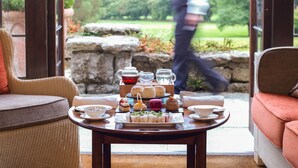 A table set with a variety of sandwiches, pastries, and beverages, with a scenic outdoor view in the background. - Gidleigh Park (Newton Abbot)