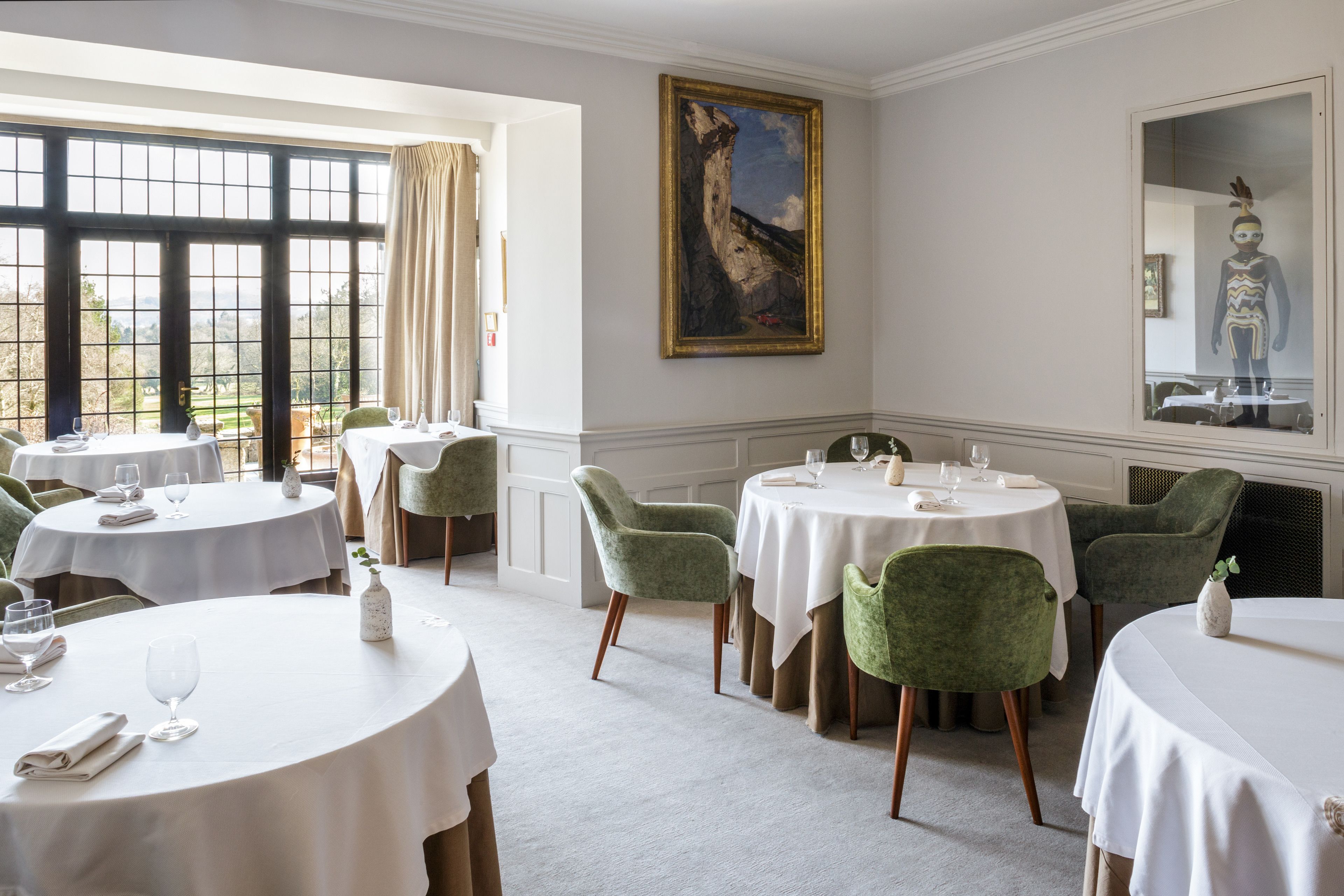A dining area with round tables, green upholstered chairs, and a large window with a view.