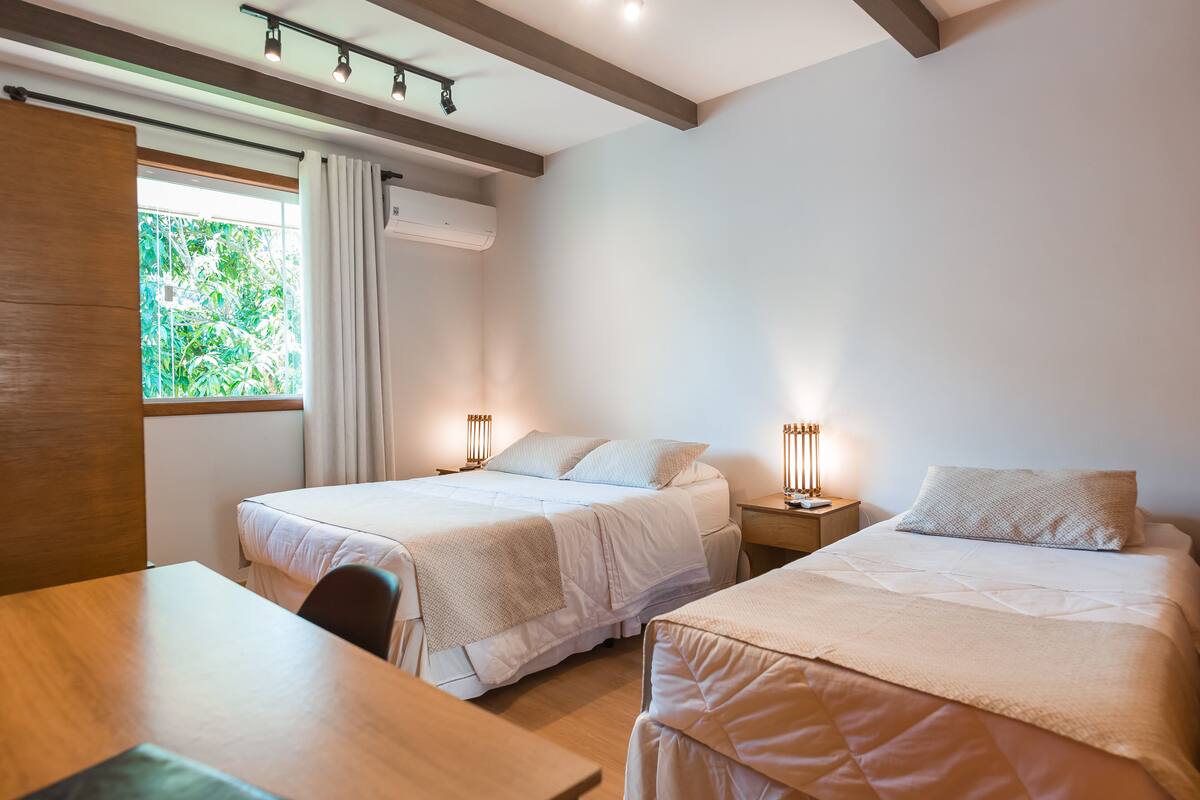 A hotel room with two beds, a wooden table, and a window with curtains.