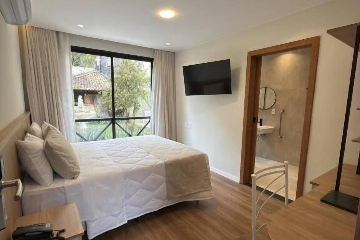 A modern hotel room with a bed, a desk, a chair, a TV, and a bathroom with a shower.