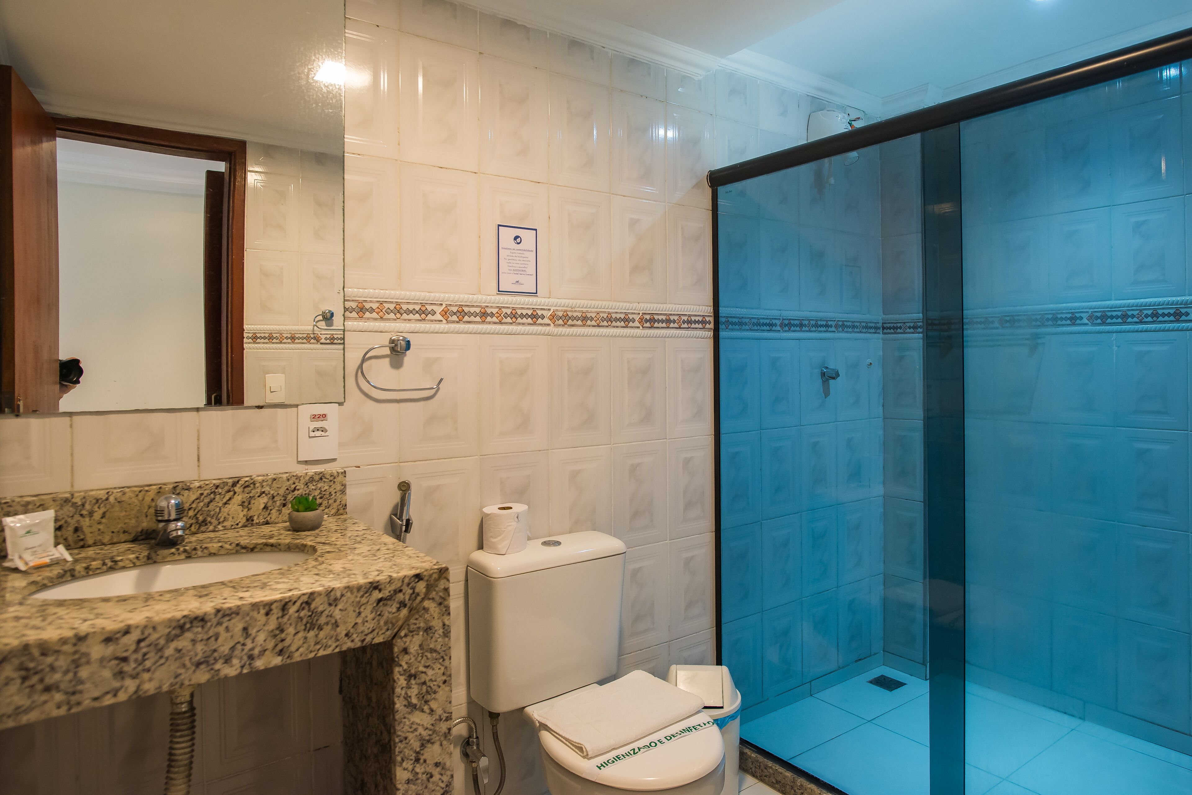 Un baño con encimera de granito, inodoro y ducha con mampara de vidrio.