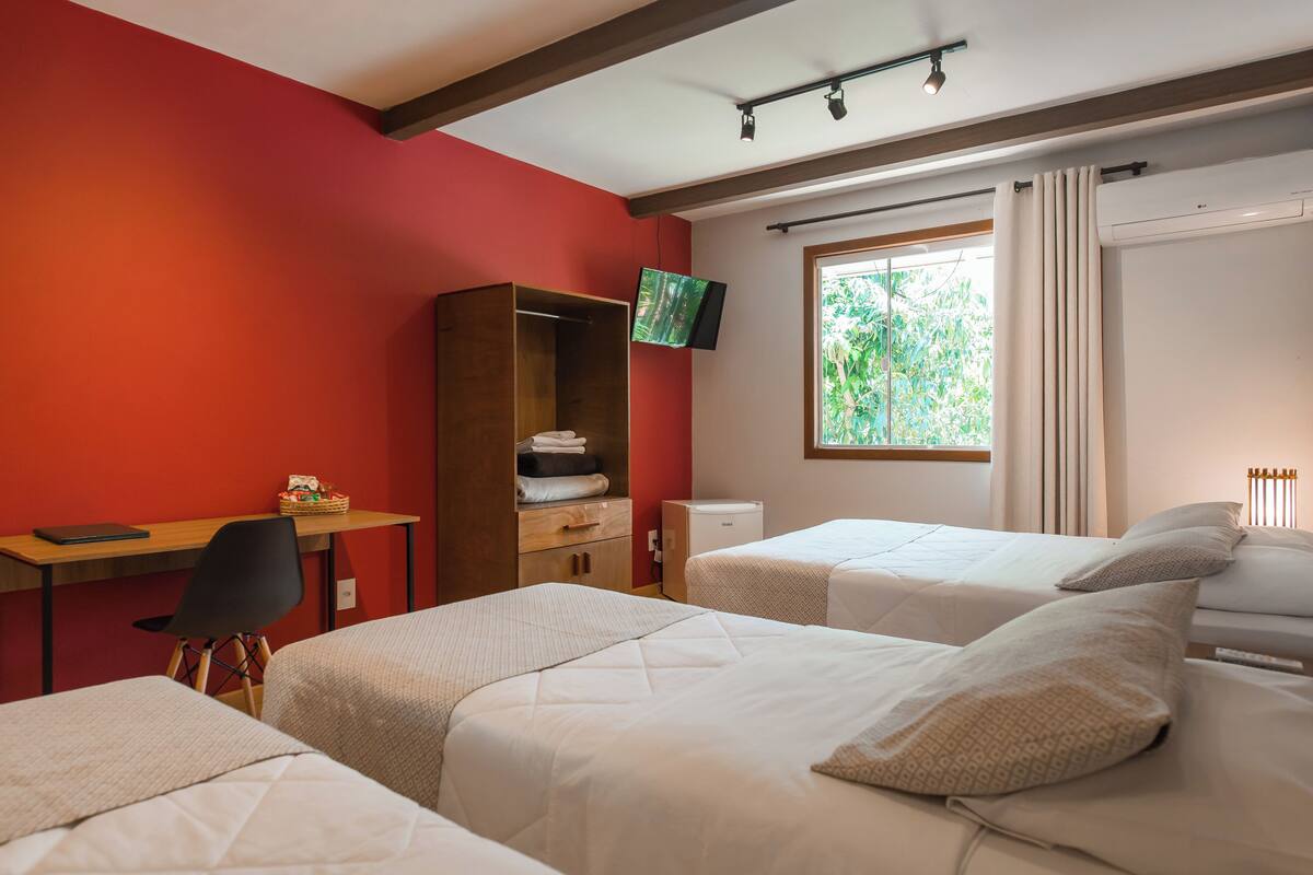 A hotel room with two beds, a desk, a TV, and a window with curtains.