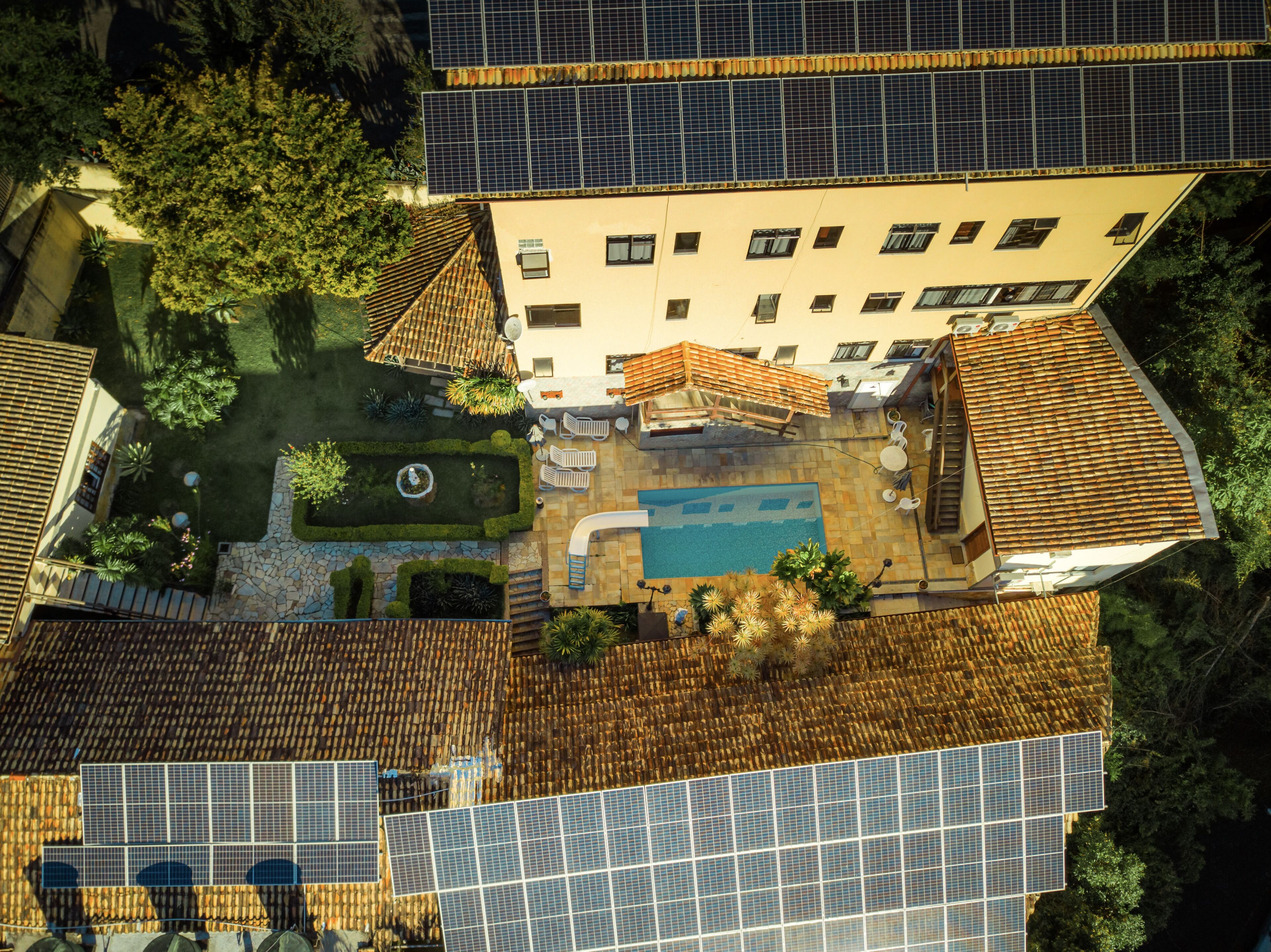 Vista aérea de un edificio con paneles solares, piscina y jardín.