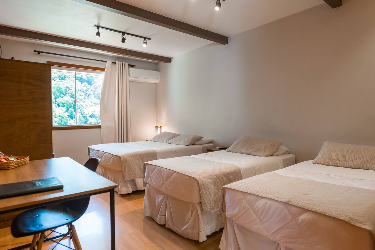 A room with two single beds, a wooden desk, a chair, and a window with curtains.