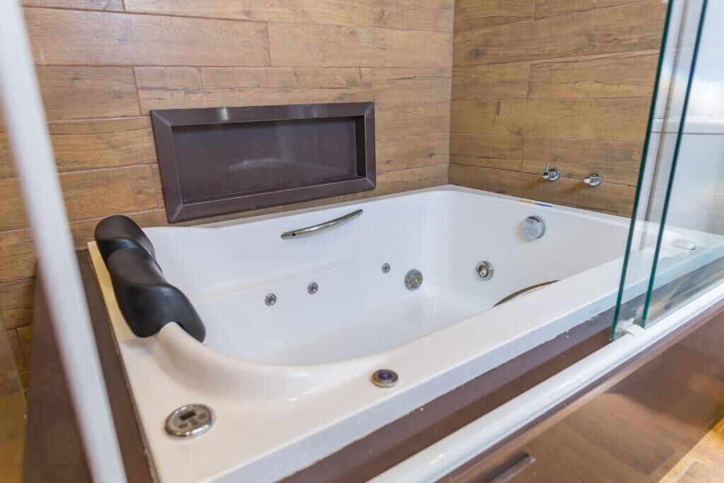 A modern bathroom with a glass-enclosed bathtub, wooden panel walls, and a built-in shelf above the tub.