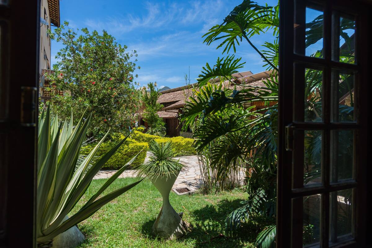 A garden with a variety of plants and a thatched-roof building in the background.