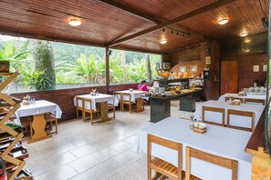 A restaurant with wooden tables and chairs, a buffet area, and large windows overlooking a lush garden.