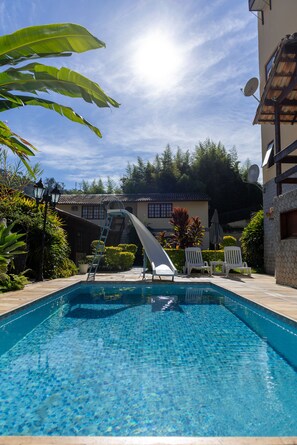A swimming pool with a slide, surrounded by lounge chairs and potted plants.
