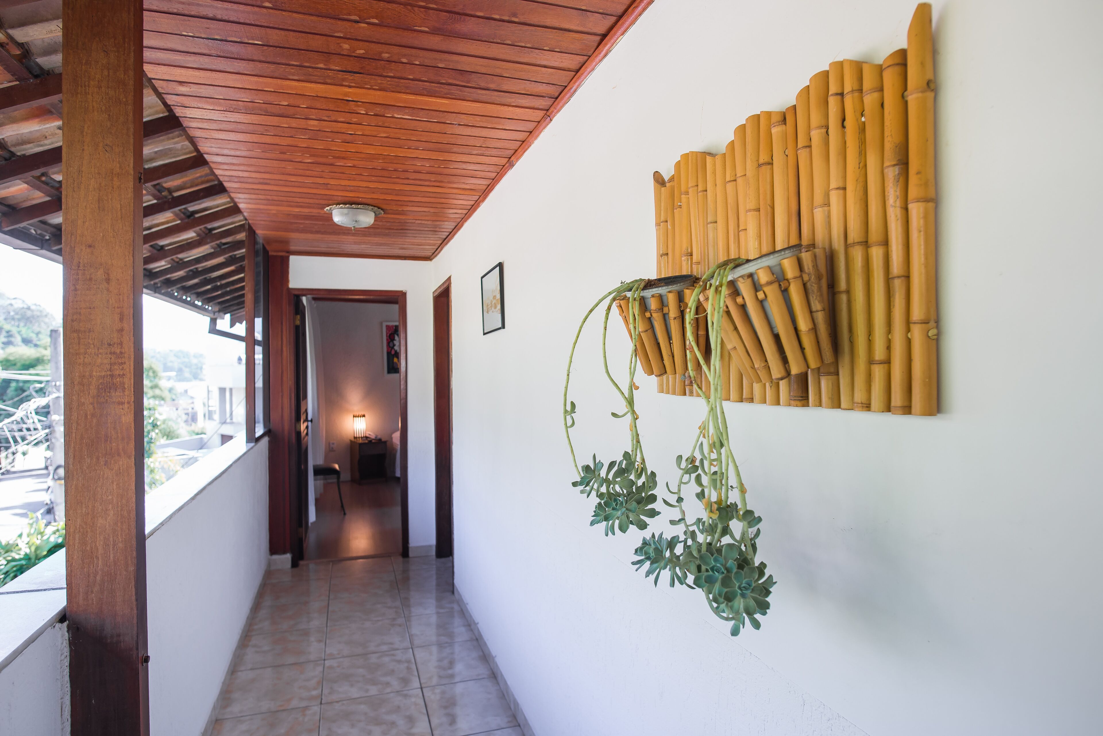 A corridor with a wooden ceiling, a bamboo wall decoration, and a hanging plant.