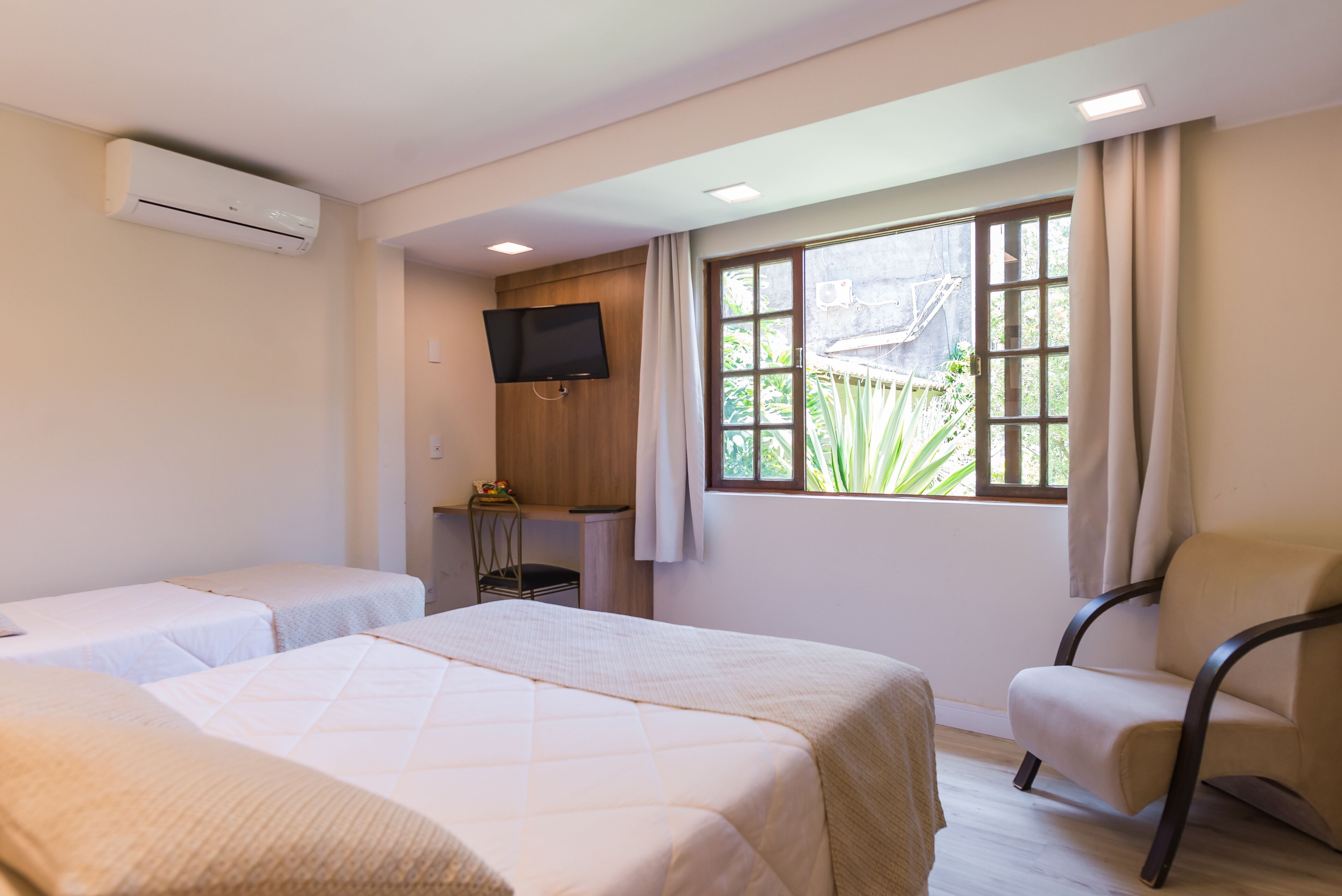 A hotel room with two beds, a TV, a desk, and a window with curtains.