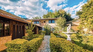 A courtyard with a stone pathway, neatly trimmed hedges, and a fountain.
