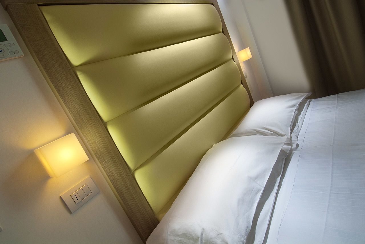 Ein Hotelzimmer mit Kopfteil, Bett, Wandleuchte und Steckdose.