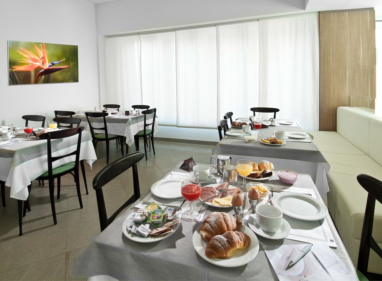Uma área de refeições com mesas preparadas para o café da manhã, incluindo pratos de comida, bebidas e diversas opções para o café.