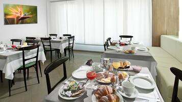 Uma área de refeições com mesas preparadas para o café da manhã, incluindo pratos de comida, bebidas e diversas opções para o café.