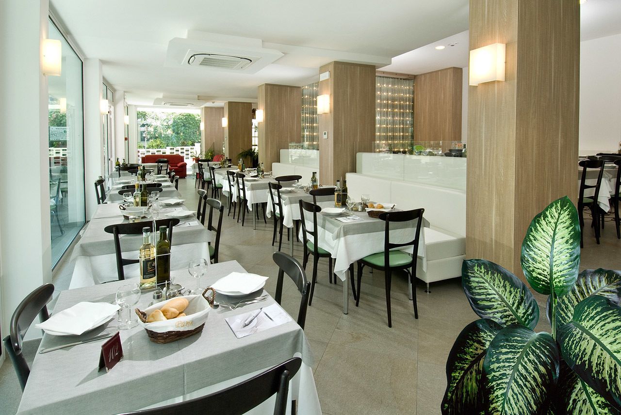 A restaurant with multiple tables, chairs, and a large plant in the foreground.
