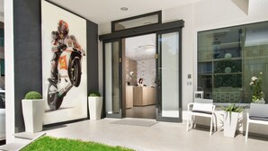 A modern reception area with a large motorcycle advertisement, a reception desk, and a seating area with potted plants. - Hotel Atlantic (Gabicce Mare)