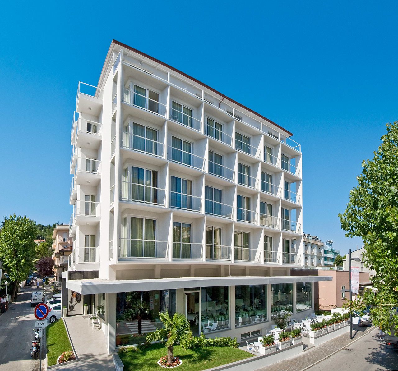 A modern multi-story hotel with a flat facade, large windows, and a covered outdoor seating area.