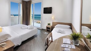 A hotel room with two beds, a desk, a chair, a TV, and a view of the beach. - Hotel Atlantic (Gabicce Mare)