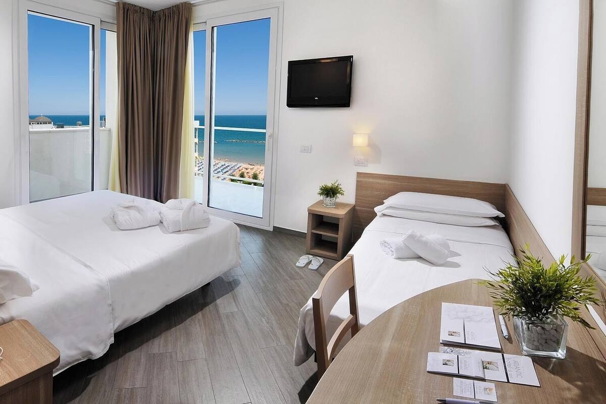 Habitación de hotel con dos camas, un escritorio, una silla, un televisor y vistas a la playa.