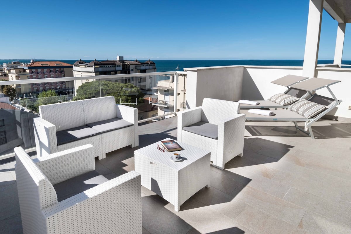 Una terraza en la azotea con mobiliario de mimbre blanco, una mesa de centro y vistas al mar.