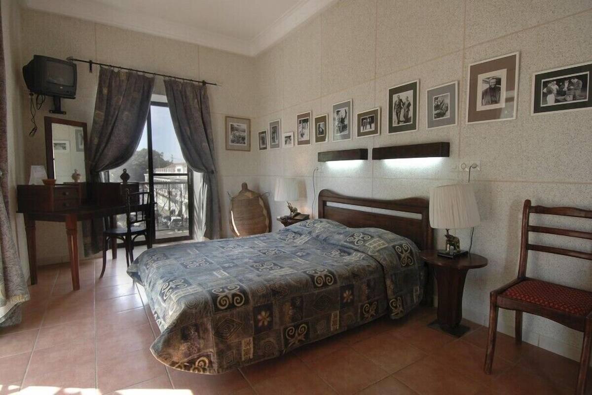 A bedroom with a bed, a desk, a chair, a television, and a balcony.