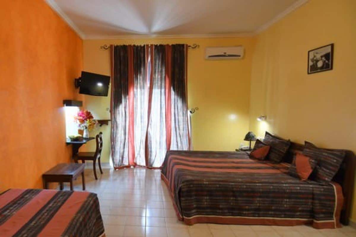 A hotel room with two beds, a desk, a chair, a TV, and a window with curtains.
