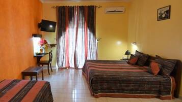 A hotel room with two beds, a desk, a chair, a TV, and a window with curtains.