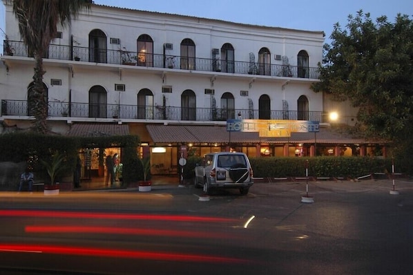 Un hotel con fachada blanca, varios balcones y un letrero que indica que es hotel y oficina de correos.